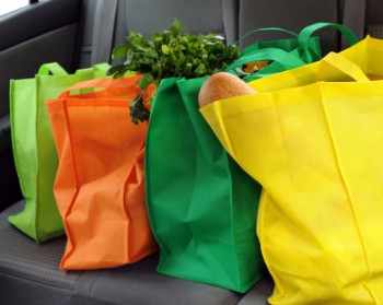 Four colorful eco-friendly shopping bags filled mostly with groceries in the back seat of a car.